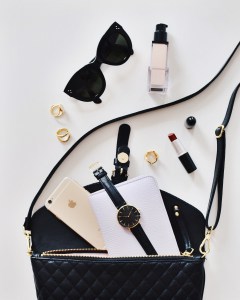 Black purse with contents spilled out, including sunglasses, lipstick, perfume, and a watch.