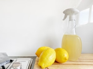 Spray bottle filled with vinegar cleaning solution and two lemons next to it.